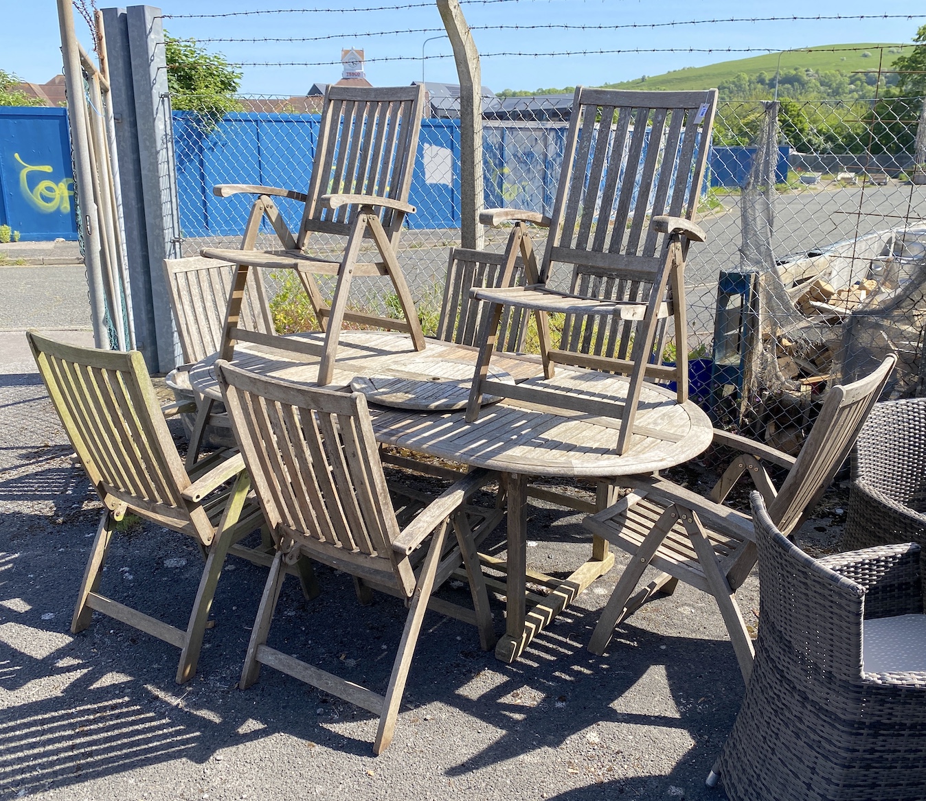 A weathered teak oval extending dining table and eight folding elbow chairs (7 plus 1), table 208cm extended, depth 110cm, height 76cm